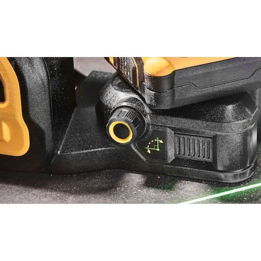 Close-up view of a DEWALT laser level adjustment knob and base, showing a yellow and black design with a control dial and an angle adjustment indicator. A green laser line is visible on the surface below.