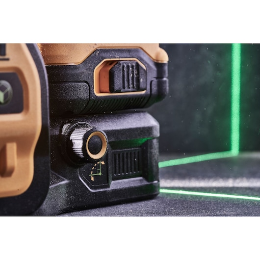 Close-up view of a DEWALT laser level device showing its adjustment knob and part of the casing, with bright green laser lines projected on a dark surface.