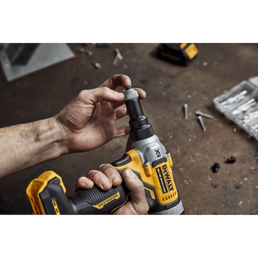 Close-up of a person's hands using a DEWALT brushless impact driver on a workbench, surrounded by screws and tool accessories.
