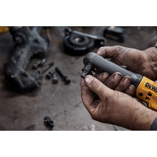 Close-up of a person with dirty hands holding a DEWALT cordless ratchet tool, surrounded by bolts and mechanical parts on a workbench.