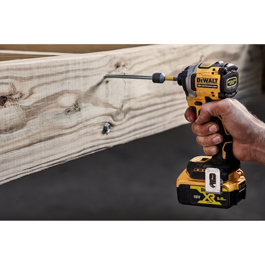 A person uses a DEWALT DCF850N 18V cordless impact driver to drive a screw into a wooden beam.