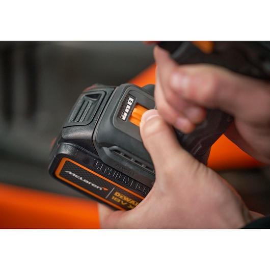 Close-up of hands holding a DEWALT cordless power tool with a McLaren branded 18V lithium battery, focusing on the battery indicator and release button.