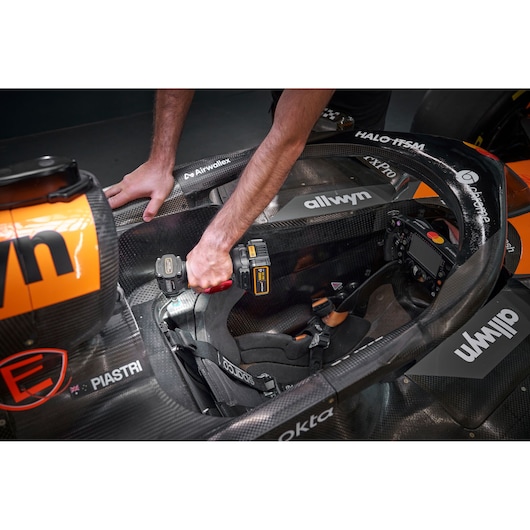 A person using a DEWALT cordless drill to work on a component inside a race car cockpit. The cockpit features branded elements with logos and a racing seat.