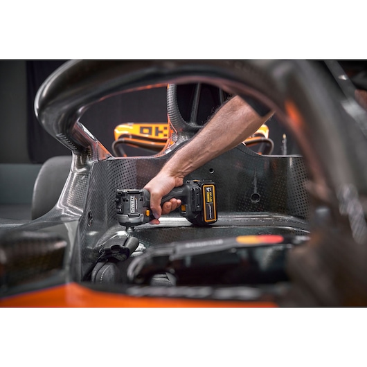 A person is using a DEWALT cordless tool inside the cockpit of a racing car, working on a carbon fiber surface.