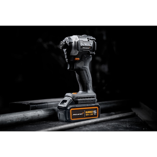 A DEWALT cordless impact driver with 18V XR 5.0Ah battery, featuring McLaren branding, displayed on a dark industrial surface.
