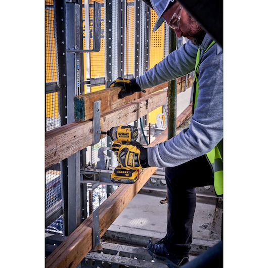 Worker using DEWALT DCF860N-XJ, DCF860N impact driver on a construction site, holding wood beams.