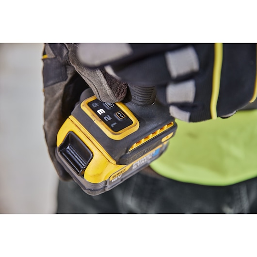 Close-up of a gloved hand operating a DEWALT cordless impact driver, SKU DCF860N, showing its control panel and speed settings.