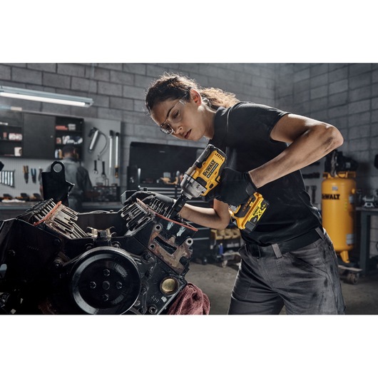 A person using a DEWALT DCF892NT cordless impact wrench to work on a large engine part in a workshop.