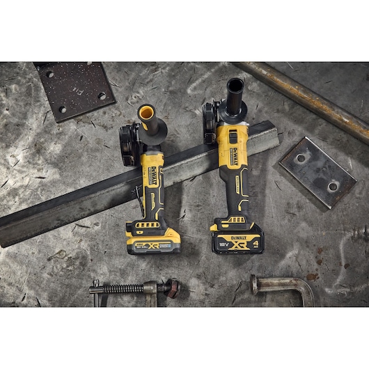 DEWALT DCG404NT and DCG404S2T-QW grinders on metal table, surrounded by metal parts.
