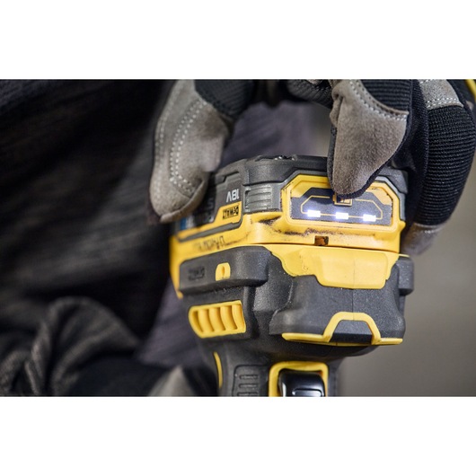 Close-up of a gloved hand pressing a button on a DEWALT cordless power tool. The LED indicator lights on the tool are illuminated.