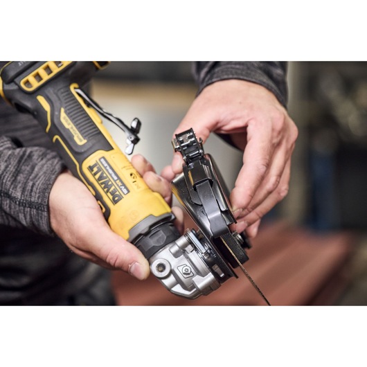 Close-up view of hands holding a DEWALT cordless angle grinder, model DCG404NT, in the process of attaching or adjusting a protective guard over the grinding wheel.