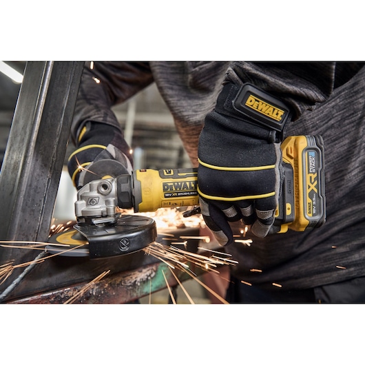 Close-up of a person wearing gloves using a DEWALT cordless angle grinder to cut metal, with sparks flying.