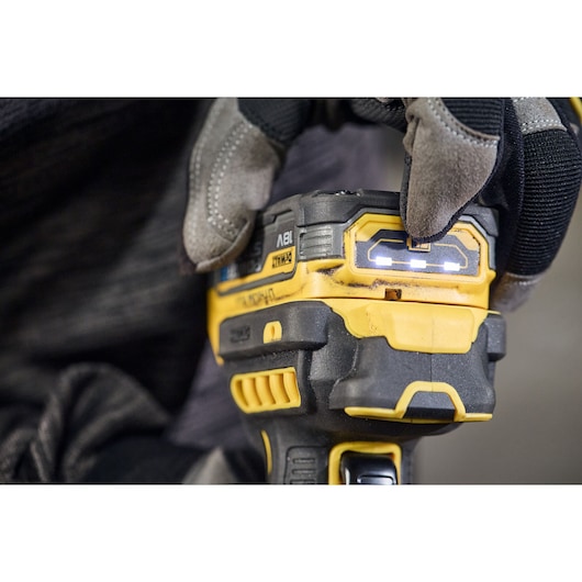 Close-up of a gloved hand operating a DEWALT cordless power tool, showing the battery indicator lights and control buttons.