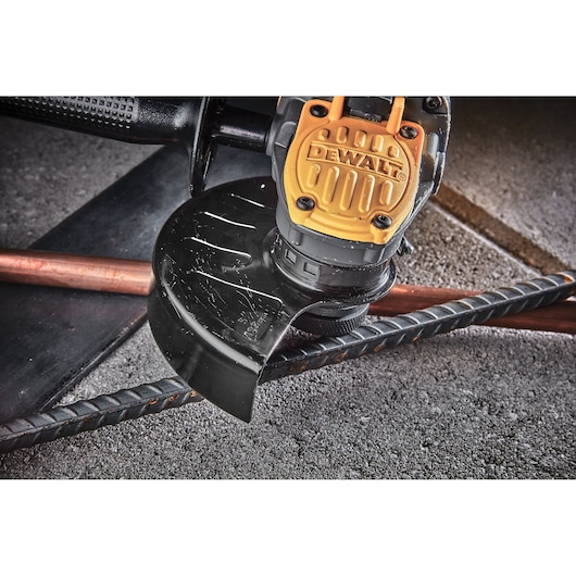 Close-up of a DEWALT angle grinder in use, cutting through metal rebar on a rough concrete surface.