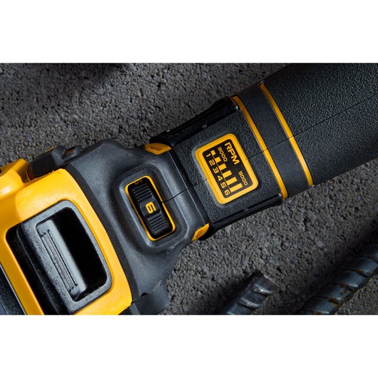 Close-up of a DEWALT power tool showing a speed control dial set to 6 and an RPM indicator label marked from 3000 to 9500. The tool features a black and yellow design and is placed on a rough concrete surface.