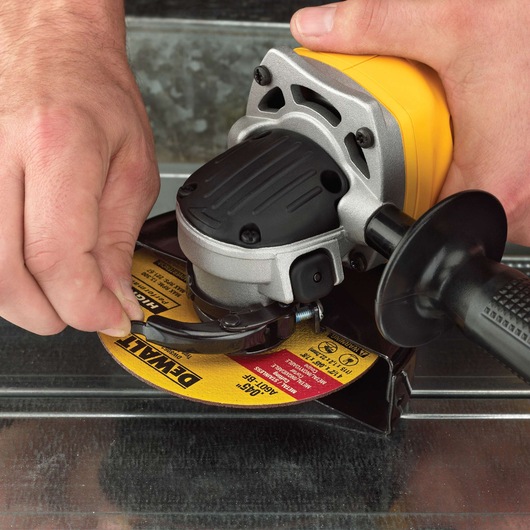 Close-up of hands adjusting the disc on a DEWALT cordless angle grinder, model DCG412M2, which is being used on a metal surface.