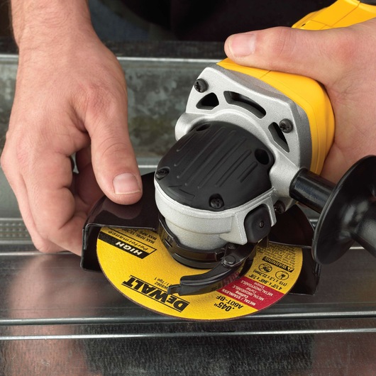 Close-up view of a person using a yellow DEWALT angle grinder with a metal grinding disc, working on a sheet of metal.