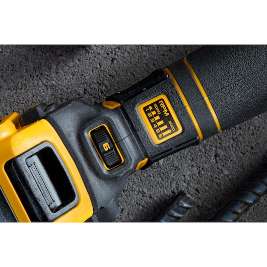 Close-up of a DEWALT power tool handle showing a speed control dial set to 6 and an RPM range label on the black and yellow grip, with the tool placed on a concrete surface.