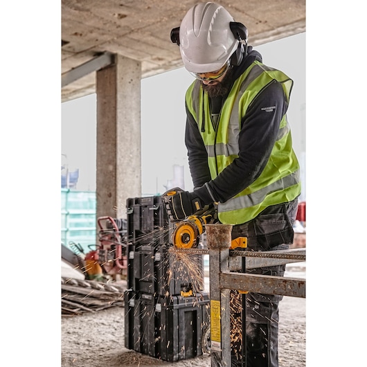Worker uses a DEWALT grinder, wearing safety gear at a construction site with sparks flying from the tool.