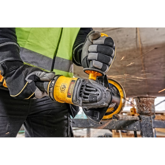 Worker uses a DEWALT angle grinder with sparks flying during metal cutting at a construction site.