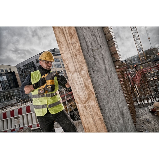 Worker uses DEWALT power tool to drill into concrete at a construction site, wearing helmet and safety vest.