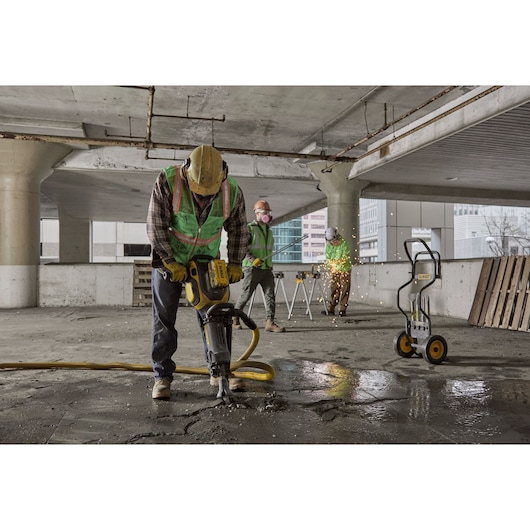 Workers use DEWALT tools for construction in a concrete building, including a jackhammer and equipment cart.