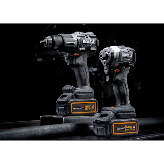 Two DEWALT cordless power tools, including a drill and an impact driver, are shown with McLaren-branded 18V XR 4.0Ah batteries. The tools are black and orange and are positioned against a dark background.