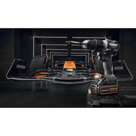 A DEWALT cordless power drill is displayed in the foreground with a black and orange formula race car in the background, set inside a modern, illuminated garage.