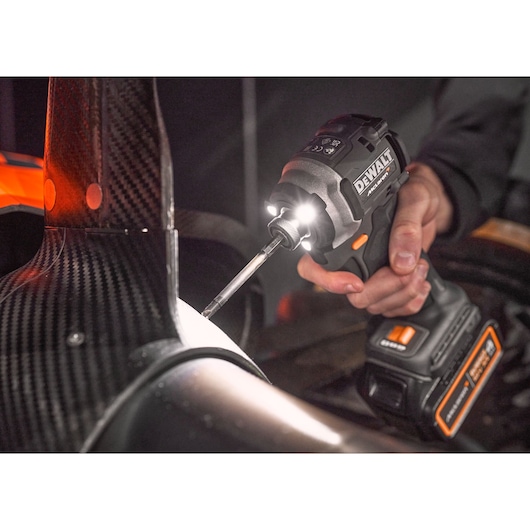 A close-up of a person using a DEWALT cordless impact driver with LED lights to fasten a screw into a carbon fiber automotive part.