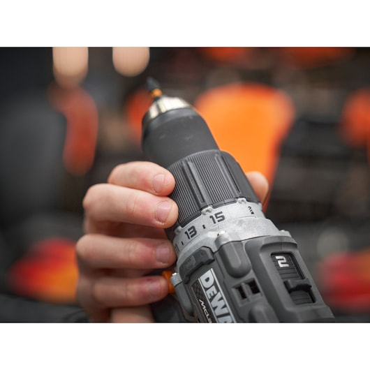 Close-up of a hand holding a DEWALT cordless power drill with visible adjustment numbers and part of the brand logo.