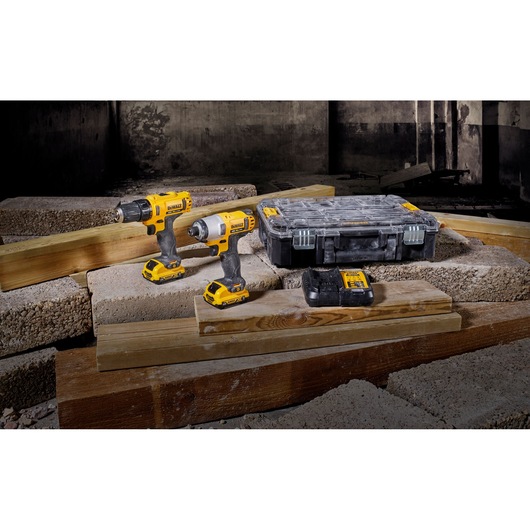 Two DEWALT cordless drills, battery, and case displayed on wooden planks and concrete blocks in a construction setting.