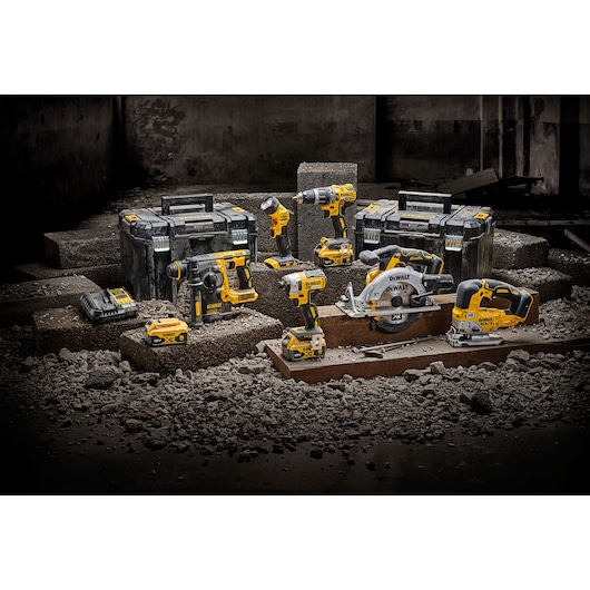 A set of yellow and black DEWALT power tools, including drills, a circular saw, a jigsaw, a rotary hammer, and battery chargers, are displayed on concrete blocks in an industrial setting. Two tool storage boxes are placed behind the tools.