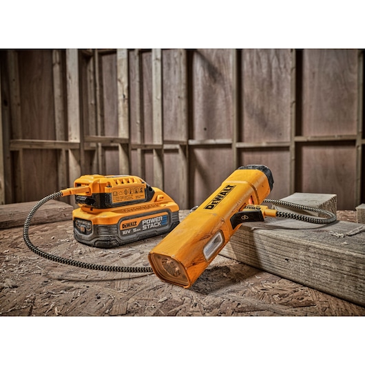 DEWALT DCL183 portable LED work light with a flexible cord, connected to a DEWALT POWERSTACK 18V battery, placed on a wooden surface in a construction setting.