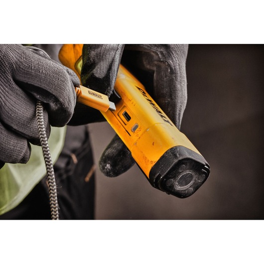 Close-up of a gloved hand plugging a USB cable into a yellow DEWALT DCL183 portable work light.