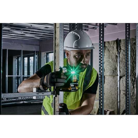 DEWALT laser level used by a worker in safety gear for construction alignment inside a building.