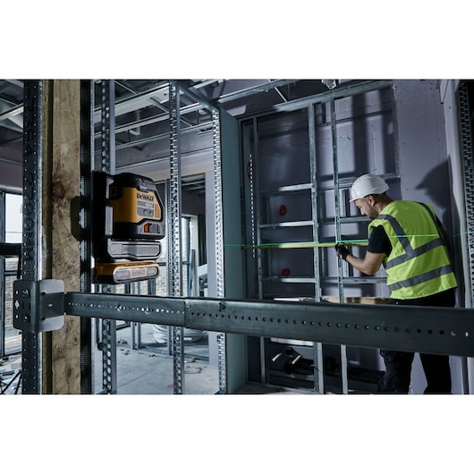 DEWALT laser level used at a construction site, worker in safety gear measuring distance with green laser line.