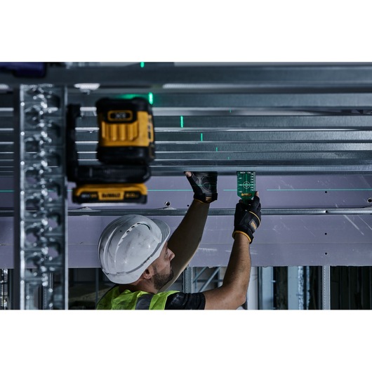 Worker uses DEWALT laser level DCLE34021 for construction alignment on metal beams.