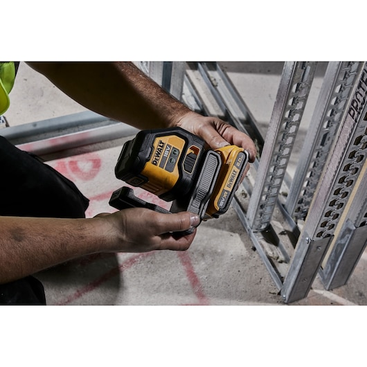 Person holds a DEWALT laser level near metal framing on a construction site floor.