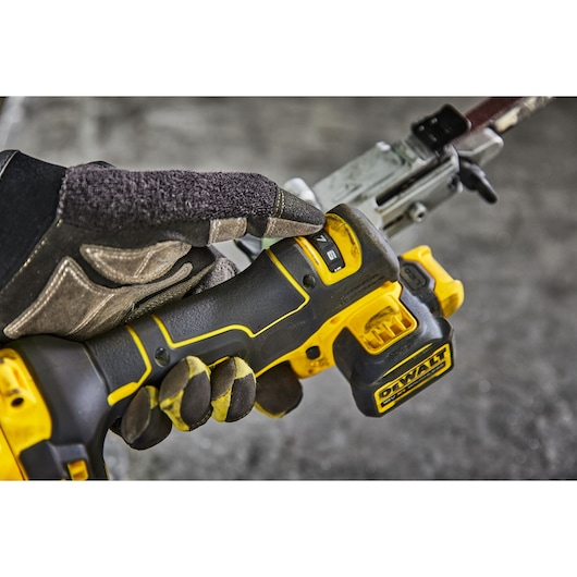 Close-up of a gloved hand operating a DEWALT cordless power tool, showing the control buttons and battery pack.