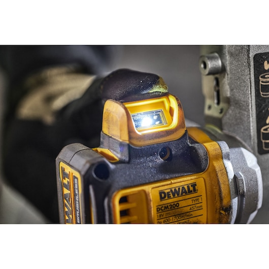 Close-up of a DEWALT DCM200 power tool in use, showing its illuminated digital display and part of its control panel. A gloved hand is operating the tool, and the DEWALT branding is visible on the body.