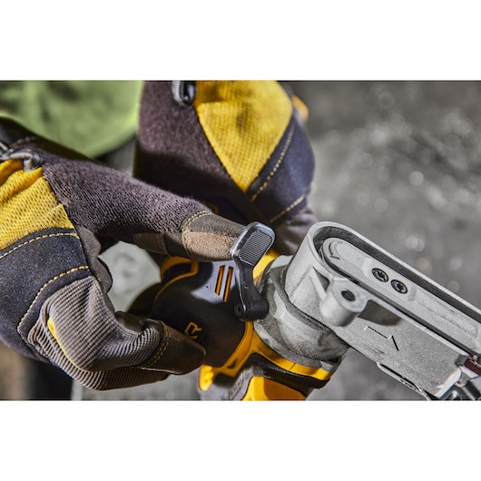 Close-up of a person wearing yellow and black gloves adjusting a control lever on a DEWALT power tool, possibly a belt sander, in a workshop setting.