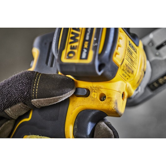 Close-up view of a gloved hand operating a yellow and black DEWALT power tool, showing the details of the tool’s switch and battery compartment.