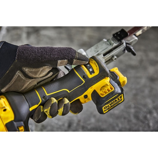 A close-up view of a gloved hand adjusting the settings on a yellow and black DEWALT cordless power tool with visible controls, battery pack, and part of a metal attachment.