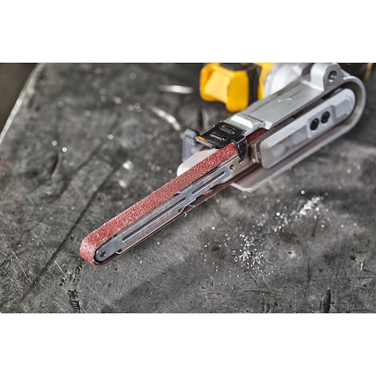 Close-up of a DEWALT cordless file belt sander with a red sanding belt on a metal work surface.