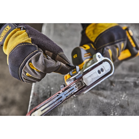 Close-up image of a person wearing DEWALT branded gloves adjusting or working with a DEWALT power tool, specifically a belt sander, on a work surface.
