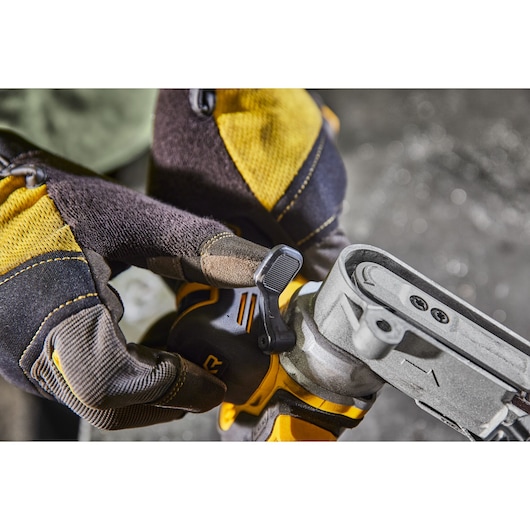 Close-up of a person wearing yellow and black gloves operating a DEWALT power tool, specifically adjusting a lever on a belt sander.