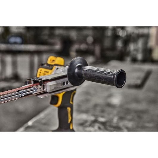 Close-up of a DEWALT handheld power tool with a sanding belt attachment, featuring a black handle and yellow accents, placed on a workshop table.