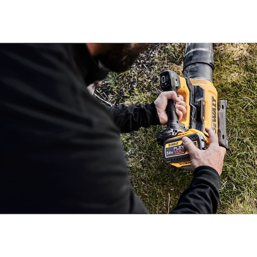 A person using a DEWALT 54V FLEXVOLT cordless blower outdoors on grass.