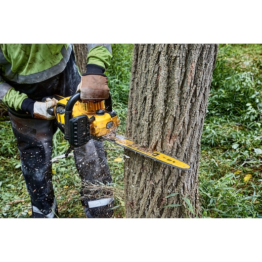A person using a yellow DEWALT chainsaw to cut through a tree trunk outdoors, wearing protective gloves and clothing.