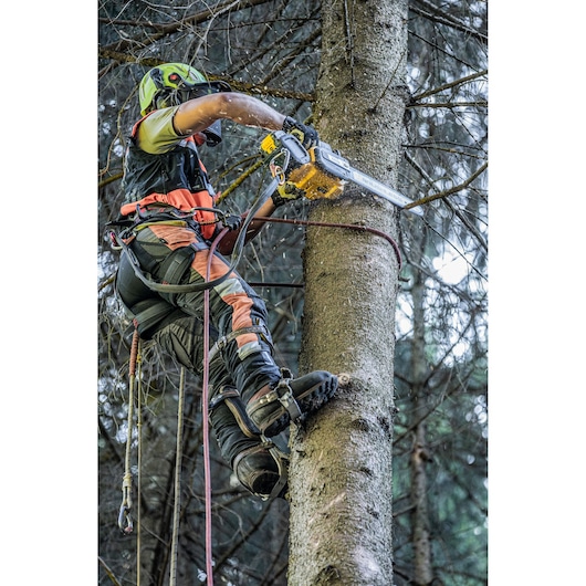A person wearing safety gear and climbing equipment is using a DEWALT chainsaw to cut a tree trunk while suspended in a forest.